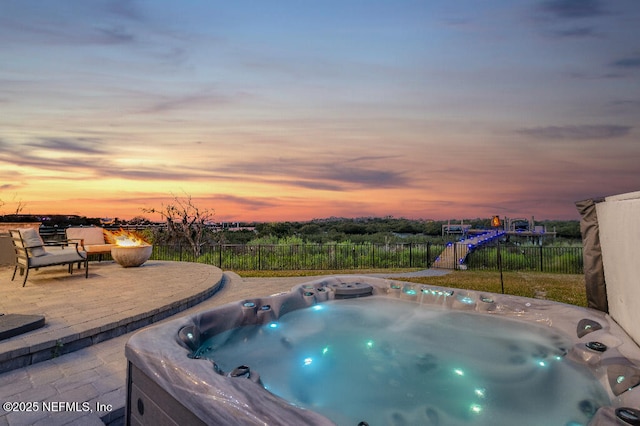 pool at dusk featuring a patio area, fence, and a hot tub