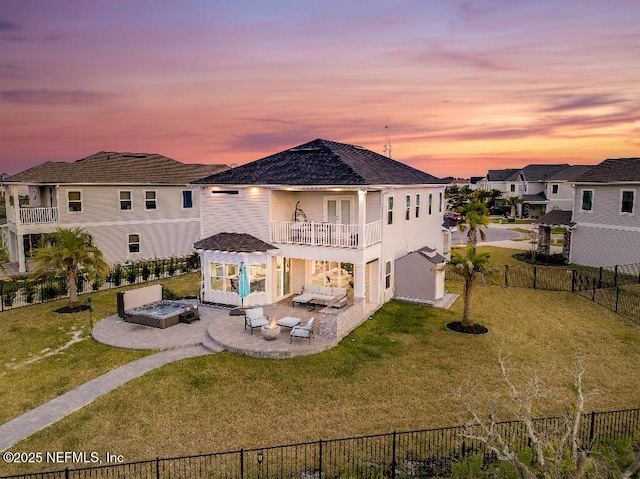 back of property at dusk featuring a fenced backyard, a balcony, a fire pit, a lawn, and a patio area