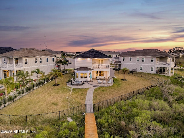 back of house at dusk featuring a yard, a residential view, a fenced backyard, and a balcony