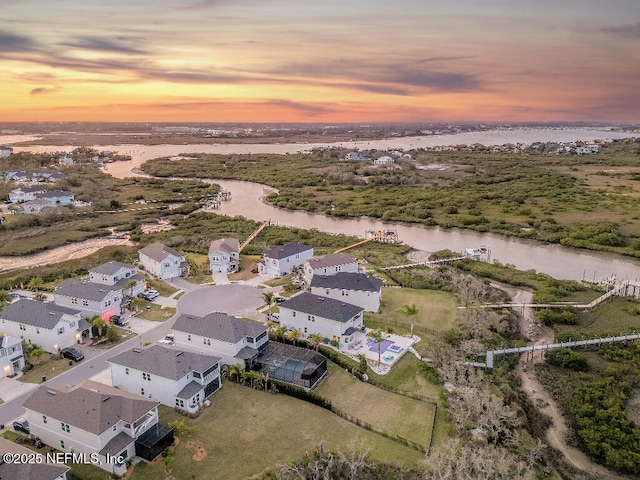 aerial view at dusk featuring a water view and a residential view