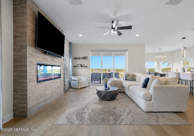 living room with a textured ceiling, ceiling fan, a glass covered fireplace, and visible vents