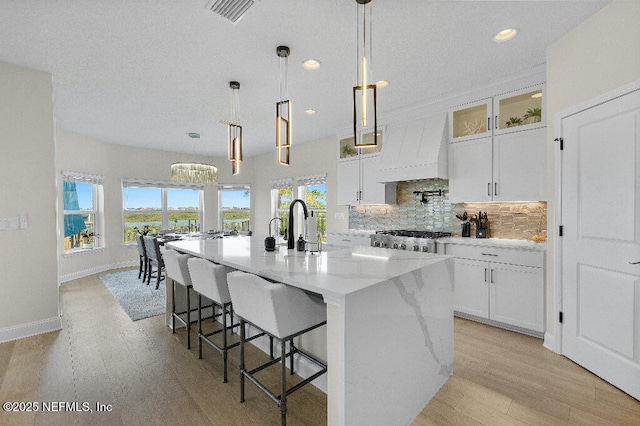 kitchen featuring light wood finished floors, visible vents, backsplash, a kitchen island with sink, and range