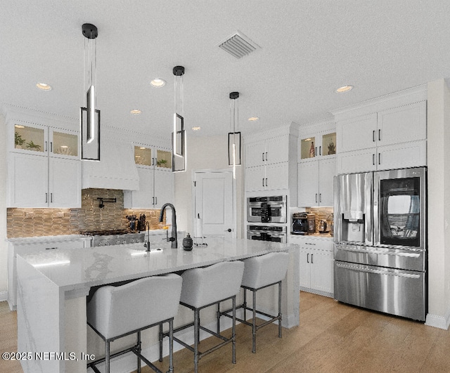 kitchen with stainless steel appliances, visible vents, glass insert cabinets, and white cabinetry