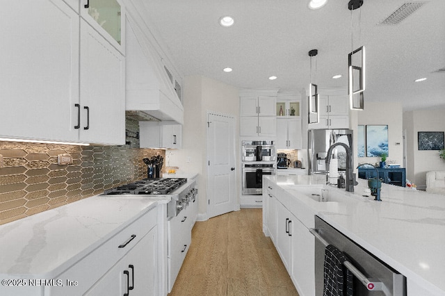 kitchen featuring hanging light fixtures, decorative backsplash, appliances with stainless steel finishes, glass insert cabinets, and white cabinets