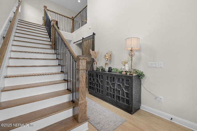 staircase with a barn door, wood finished floors, a towering ceiling, and baseboards