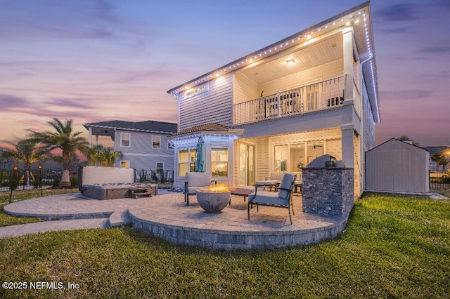 back of property at dusk featuring a patio, an outdoor fire pit, a balcony, an outdoor structure, and a shed