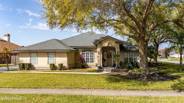 view of front of property featuring a shingled roof, a front yard, and stucco siding