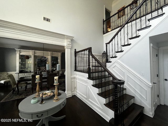 stairs with a decorative wall, wainscoting, a high ceiling, and visible vents