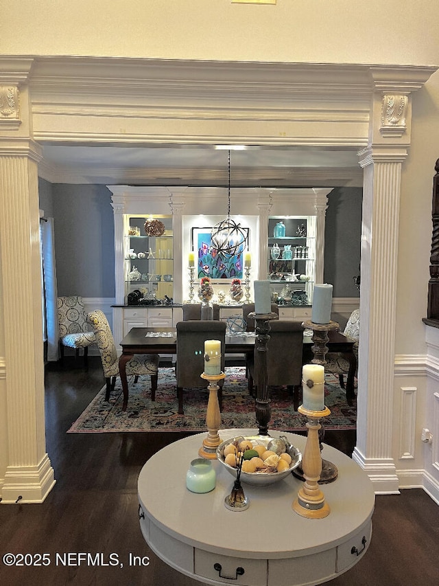 dining room featuring a decorative wall, wood finished floors, wainscoting, and ornate columns