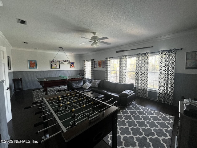 living area featuring visible vents, ornamental molding, a textured ceiling, and a wainscoted wall