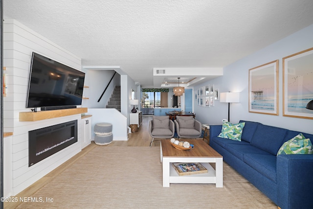 living area with light wood-type flooring, visible vents, a textured ceiling, a glass covered fireplace, and stairway