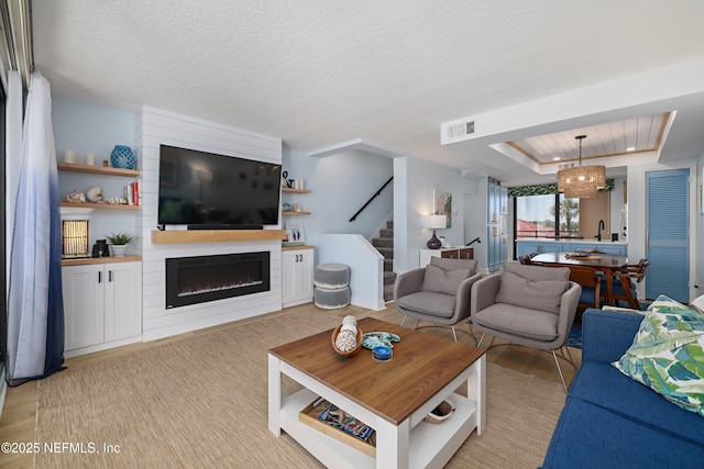 living area with visible vents, a textured ceiling, a fireplace, a raised ceiling, and stairs