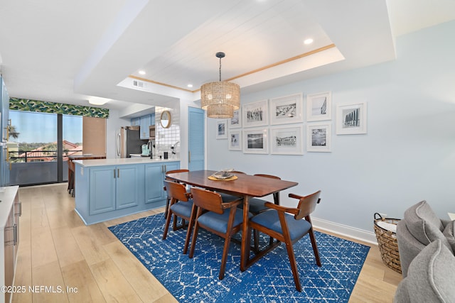 dining room with baseboards, visible vents, light wood-style floors, a raised ceiling, and a chandelier