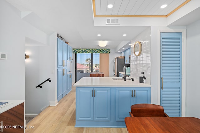 kitchen with a peninsula, blue cabinetry, a sink, light wood-type flooring, and backsplash