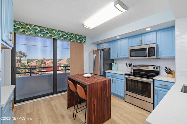 kitchen featuring light stone counters, appliances with stainless steel finishes, light wood-style floors, a textured ceiling, and blue cabinets