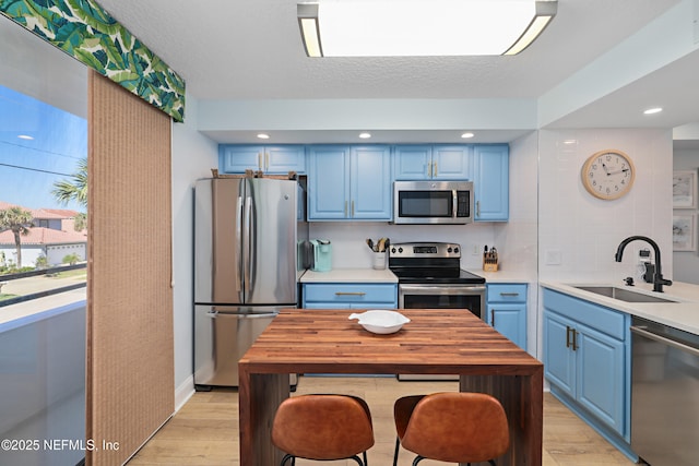 kitchen featuring light wood-style flooring, appliances with stainless steel finishes, blue cabinets, and a sink