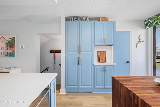 kitchen featuring tasteful backsplash, blue cabinetry, light wood-style floors, a textured ceiling, and wood counters