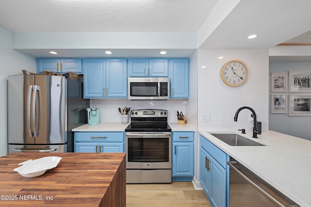 kitchen with a sink, decorative backsplash, stainless steel appliances, blue cabinets, and butcher block counters