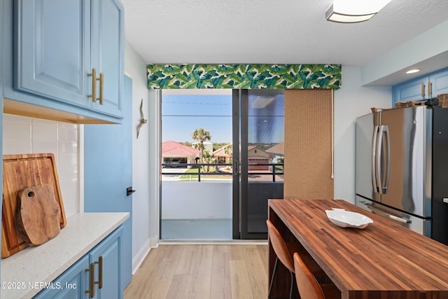 kitchen featuring blue cabinetry, freestanding refrigerator, a textured ceiling, wood counters, and light wood-type flooring