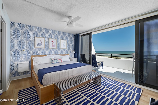 bedroom with wallpapered walls, wood finished floors, a water view, and a textured ceiling