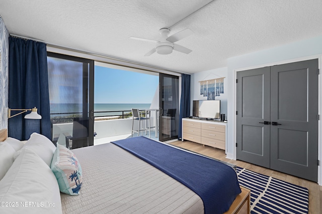 bedroom with a ceiling fan, light wood-style flooring, floor to ceiling windows, and a textured ceiling