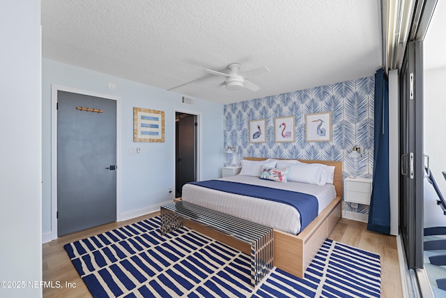 bedroom with light wood-style flooring, a textured ceiling, wallpapered walls, baseboards, and an accent wall