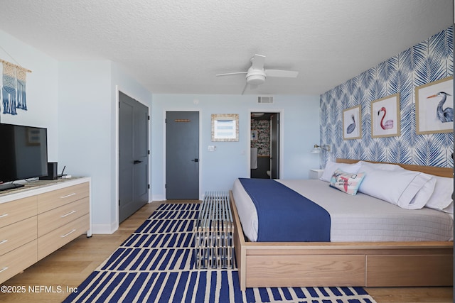 bedroom with visible vents, a textured ceiling, light wood-style floors, wallpapered walls, and an accent wall