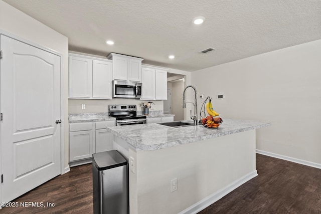 kitchen with dark wood-type flooring, a center island with sink, light countertops, stainless steel appliances, and a sink