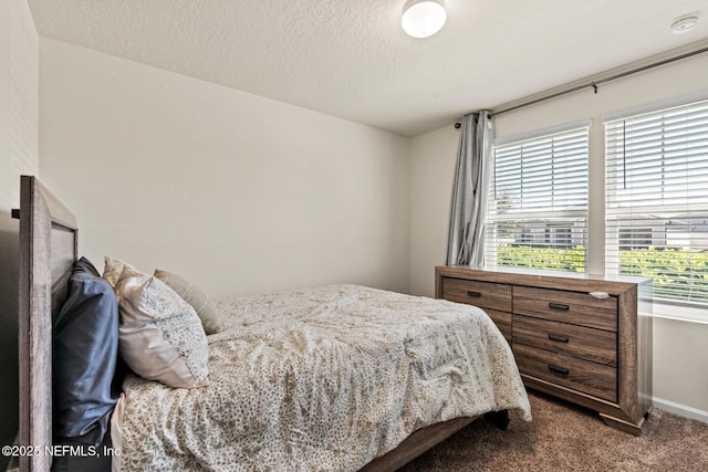 bedroom with baseboards, a textured ceiling, and dark carpet