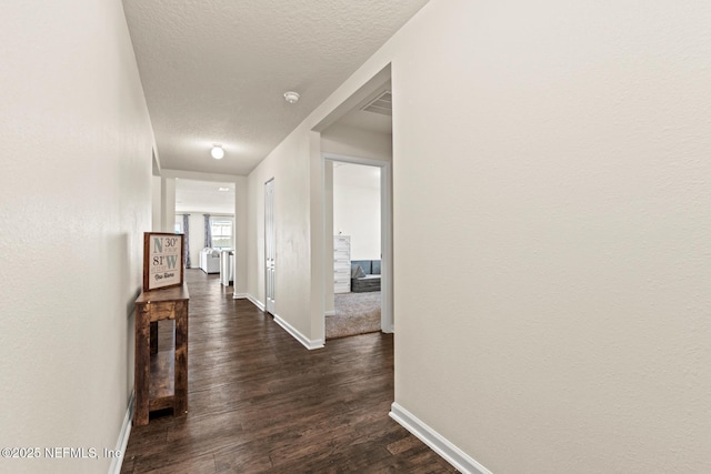 hall featuring visible vents, baseboards, dark wood-type flooring, and a textured ceiling