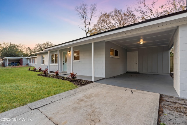 ranch-style home featuring driveway, concrete block siding, a carport, a yard, and board and batten siding