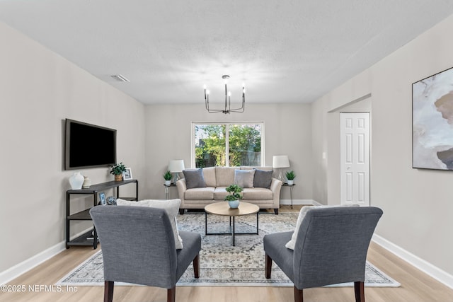 living area featuring visible vents, a textured ceiling, a chandelier, light wood-type flooring, and baseboards