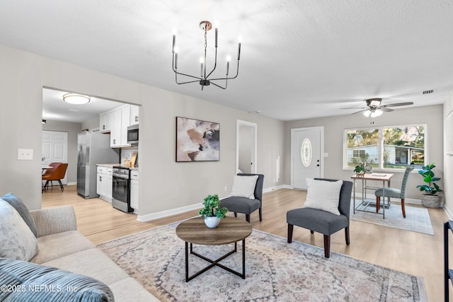 living area featuring visible vents, a textured ceiling, a chandelier, light wood-type flooring, and baseboards