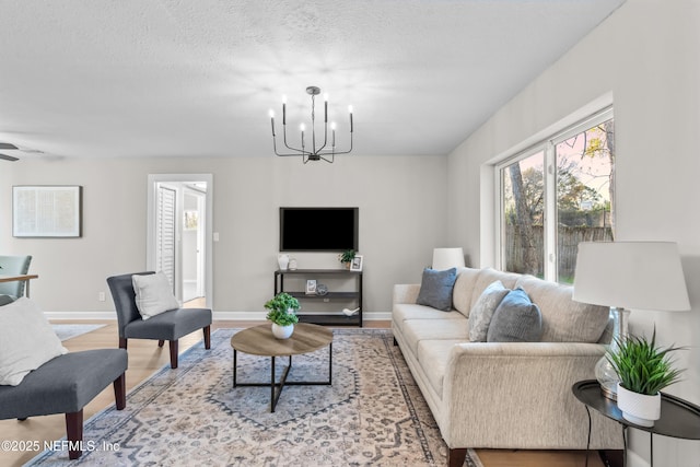 living room featuring an inviting chandelier, a textured ceiling, baseboards, and wood finished floors