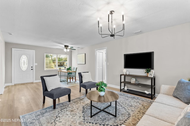 living room featuring a textured ceiling, ceiling fan with notable chandelier, visible vents, baseboards, and light wood finished floors