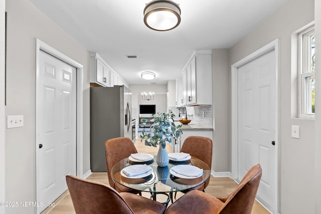 dining area featuring baseboards, light wood-style flooring, visible vents, and a notable chandelier