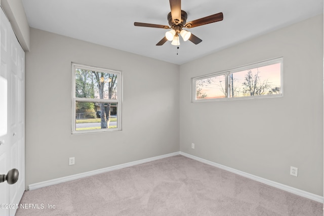 carpeted empty room featuring ceiling fan and baseboards