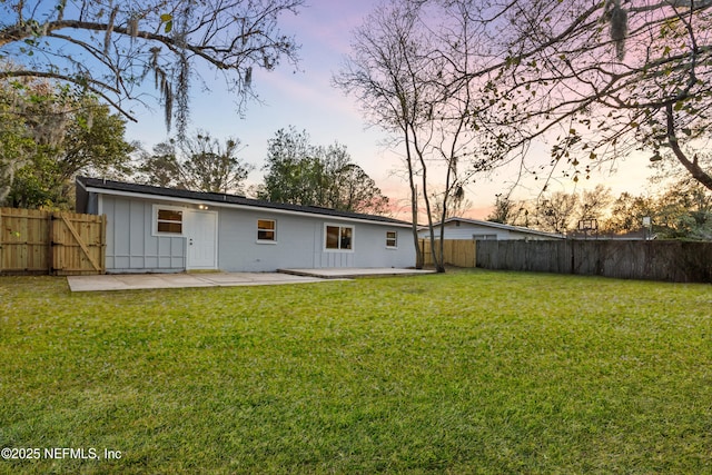 back of house featuring board and batten siding, a fenced backyard, a patio, and a lawn