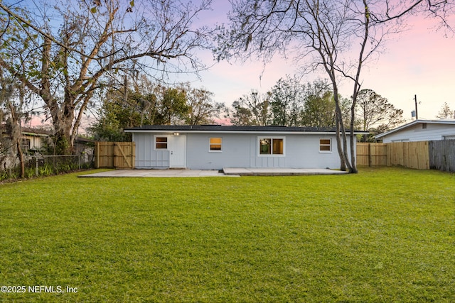 back of house at dusk featuring board and batten siding, a lawn, a patio area, and a fenced backyard