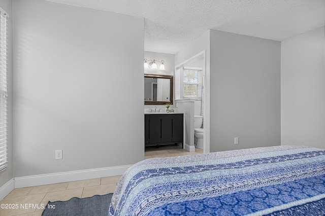 tiled bedroom featuring a textured ceiling, baseboards, ensuite bathroom, and a sink