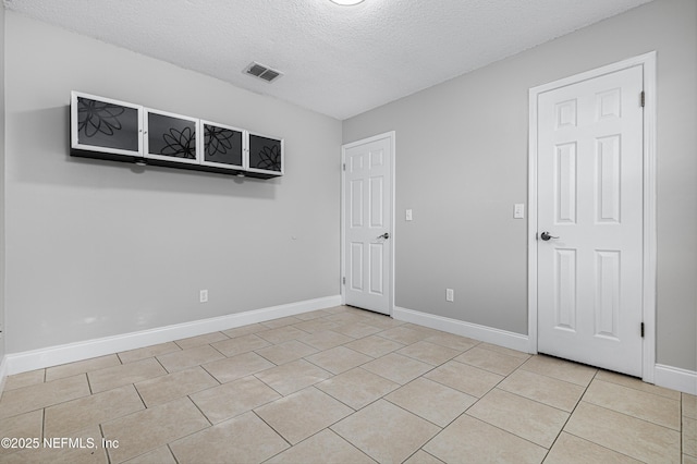 spare room with light tile patterned flooring, baseboards, visible vents, and a textured ceiling