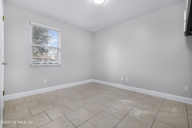 empty room featuring light tile patterned floors, baseboards, and a textured ceiling