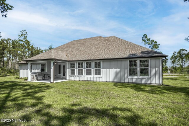 back of house with a shingled roof, board and batten siding, a patio area, and a lawn