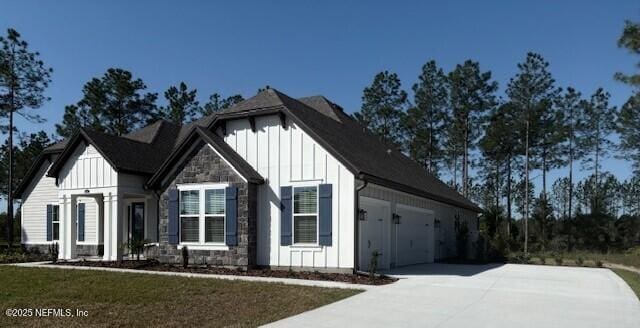 view of side of property featuring board and batten siding, an attached garage, driveway, and stone siding