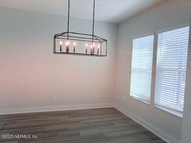 unfurnished dining area featuring a notable chandelier, baseboards, and dark wood finished floors