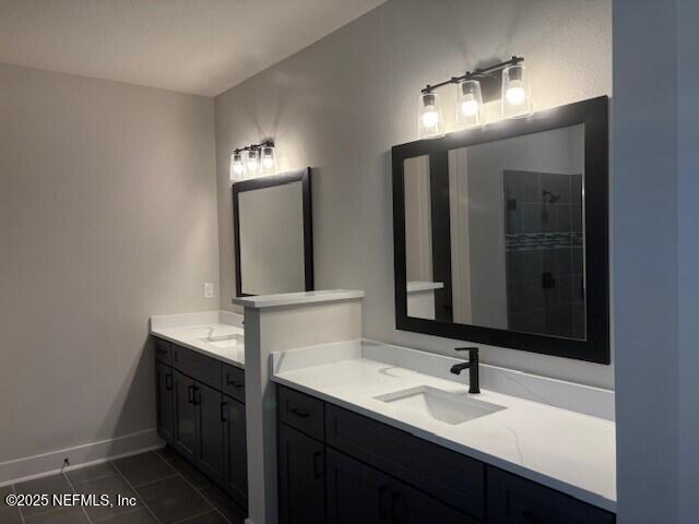 bathroom featuring baseboards, tile patterned floors, two vanities, a sink, and a tile shower