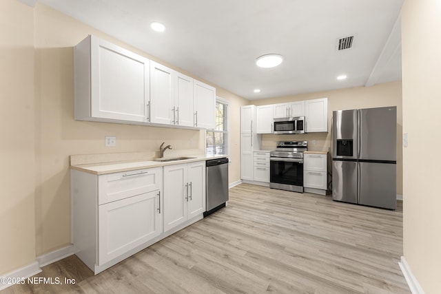 kitchen with a sink, visible vents, white cabinets, light countertops, and appliances with stainless steel finishes