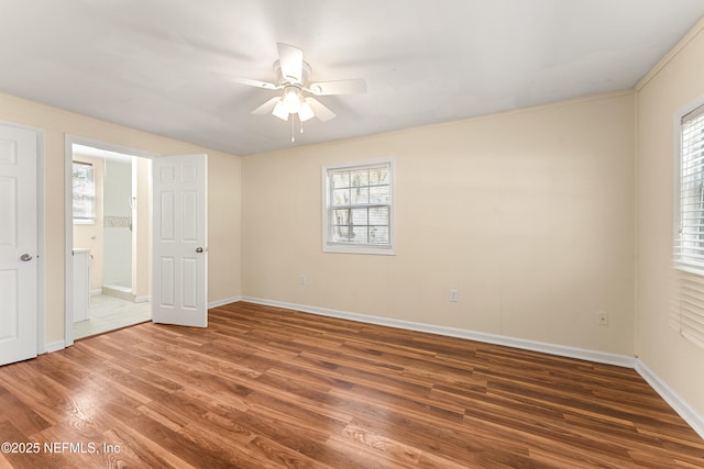 unfurnished bedroom with multiple windows, connected bathroom, baseboards, and wood finished floors