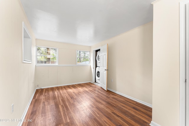 unfurnished room featuring stacked washer / drying machine, baseboards, and wood finished floors