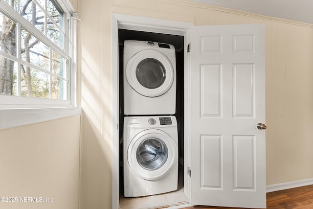 washroom featuring stacked washing maching and dryer, baseboards, laundry area, and wood finished floors